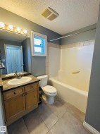 Full bathroom with a wood-finish vanity, integrated sink, and dark countertop - 
