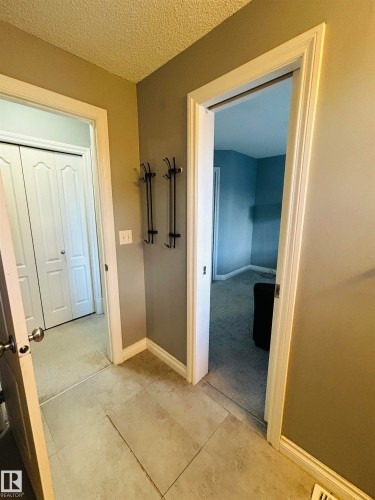 Tiled flooring entry area featuring white baseboards, textured walls, and a coat rack with four hooks - 89 12050 17 Avenue, Edmonton, AB 