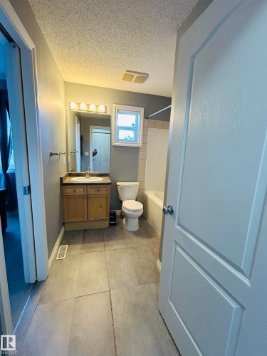 Bathroom featuring large format tile flooring, a wood-finish vanity with countertop sink, and a combination tub and shower - 89 12050 17 Avenue, Edmonton, AB 