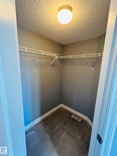 Walk-in closet featuring built-in wire shelving, neutral wall paint, and a textured ceiling with a flush-mount light fixture - 89 12050 17 Avenue, Edmonton, AB 