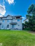 Rear exterior with siding, featuring multiple windows, a sliding glass door, a patio area, and a substantial lawn - 89 12050 17 Avenue, Edmonton, AB 
