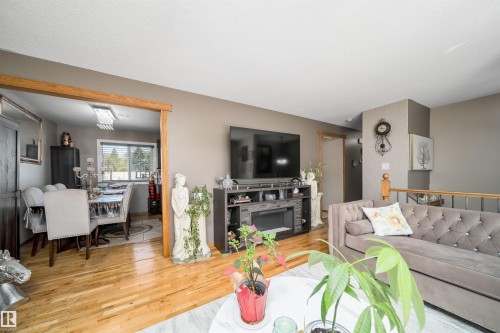 Living area featuring wood-finish flooring, a built-in media console with an electric fireplace, and an open doorway to the dining area - 14808 96 Street, Edmonton, AB 