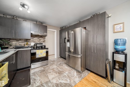 Kitchen featuring dark wood-finish cabinetry, stainless steel appliances, a multi-tone tile backsplash, and large format stone-look floor tiles - 14808 96 Street, Edmonton, AB 