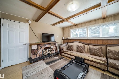 Living area featuring a stone-clad fireplace with a wood mantel, wood-finish flooring, and white paneled door - 14808 96 Street, Edmonton, AB 