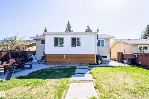 Expansive rear yard featuring a concrete patio, mature lawn, and a pathway leading to the main structure - 14808 96 Street, Edmonton, AB 