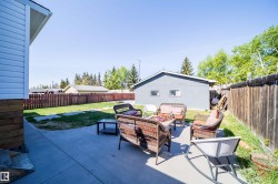 Concrete patio with surrounding lawn area, wood privacy fence, and detached garage structure - 