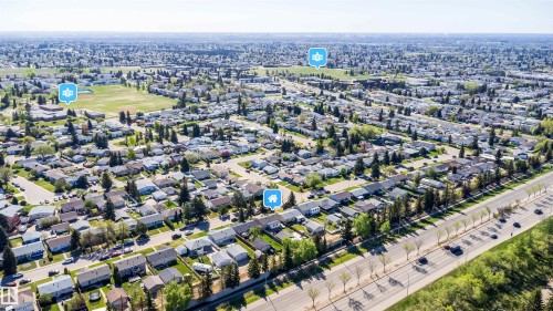 Expansive aerial perspective showcasing a residential development with numerous single-story homes, mature tree-lined streets, and a prominent multi-lane thoroughfare - 14808 96 Street, Edmonton, AB 