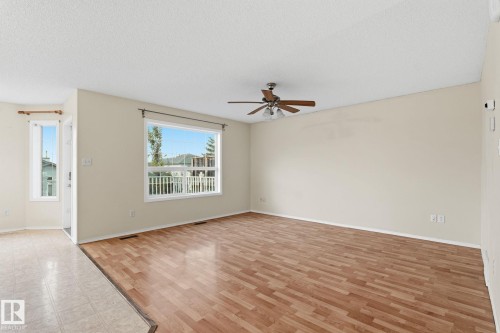 Spacious room with wood-finish flooring, a contemporary ceiling fan, and large windows providing abundant natural light - 1906 37B Av, Edmonton, AB 