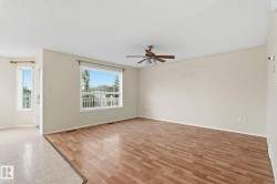 Spacious room with wood-finish flooring, a contemporary ceiling fan, and large windows providing abundant natural light - 