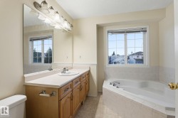 Spacious bathroom featuring a corner soaking tub, a long vanity with dual sinks, and a large mirror with integrated lighting - 