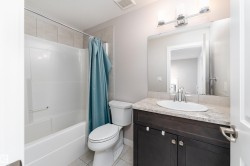 Bathroom featuring a white bathtub/shower combination with tile surround, a dark wood-finish vanity with a light-toned countertop, an oval undermount sink, and chrome fixtures - 
