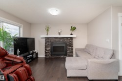 Living area featuring a stone-clad fireplace with a white mantel, dark wood-finish flooring, a large window, and a ceiling-mounted light fixture - 