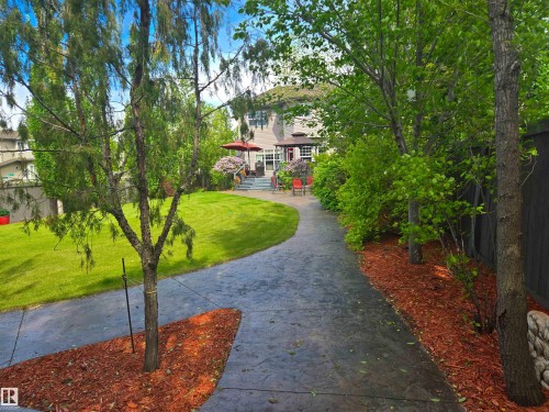 Spacious backyard featuring a stamped concrete path, manicured lawn, mature trees, and a multi-level patio - 704 Wildwood Point(E), Edmonton, AB 