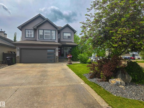 Two-story exterior with gray siding, dark trim accents, a concrete driveway, an attached garage with frosted glass panels, and mature landscaping with decorative rocks - 704 Wildwood Point(E), Edmonton, AB 