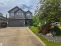 Two-story exterior with gray siding, dark trim accents, a concrete driveway, an attached garage with frosted glass panels, and mature landscaping with decorative rocks - 704 Wildwood Point(E), Edmonton, AB 