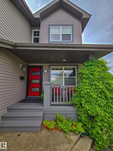 Inviting front entrance featuring a vibrant red door, covered porch, gray siding, white-framed windows, and mature greenery - 704 Wildwood Point(E), Edmonton, AB 