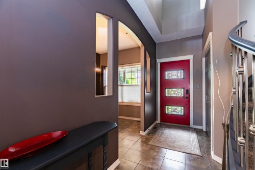 Foyer entrance featuring a vibrant red door with decorative glass inserts, tiled flooring, and an elegant curved staircase with metal railings - 704 Wildwood Point(E), Edmonton, AB 