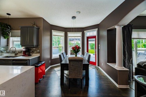Open-concept dining area featuring dark wood-finish flooring, a contemporary chandelier, bay windows, and a red exterior door - 704 Wildwood Point(E), Edmonton, AB 