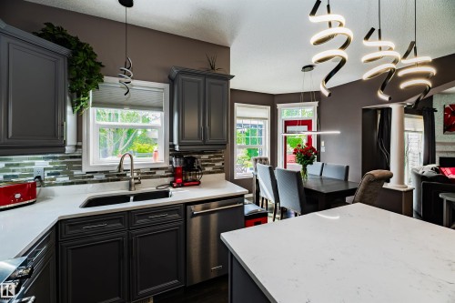 Contemporary kitchen featuring dark cabinetry, light-toned countertops, and a mosaic tile backsplash - 704 Wildwood Point(E), Edmonton, AB 