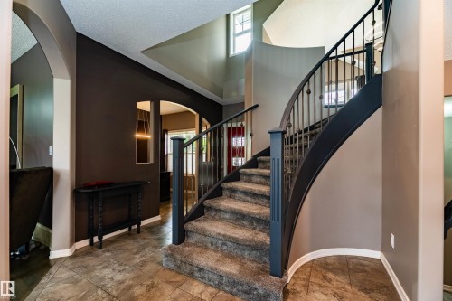 Grand entryway featuring a curved staircase with wrought iron balusters and a carpeted tread - 704 Wildwood Point(E), Edmonton, AB 