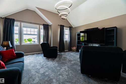 Vaulted ceiling room featuring a contemporary ring chandelier, three large window panes with horizontal muntins, wall-mounted display unit, and neutral wall paint - 704 Wildwood Point(E), Edmonton, AB 