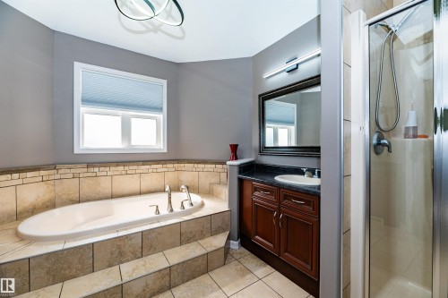 Soaking tub with a tiled surround and mosaic accents, complemented by a separate glass-enclosed shower - 704 Wildwood Point(E), Edmonton, AB 