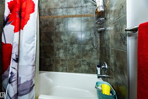Bathtub with tile surround featuring a decorative accent band and a mounted showerhead with handheld attachment - 704 Wildwood Point(E), Edmonton, AB 