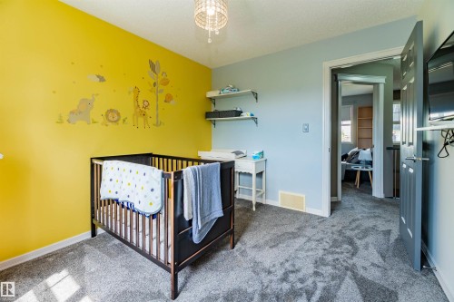 Room featuring textured gray carpeting, a textured yellow accent wall, and a crystal chandelier - 704 Wildwood Point(E), Edmonton, AB 