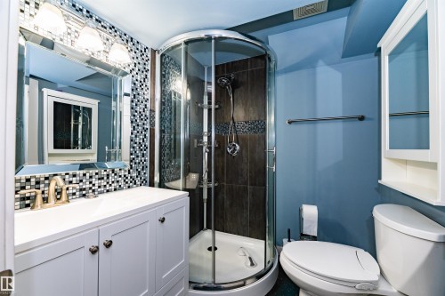 Bathroom featuring a white vanity with a rectangular sink, a framed mirror with integrated lighting, a mosaic tile backsplash, a curved glass shower enclosure, and a wall-mounted medicine cabinet - 704 Wildwood Point(E), Edmonton, AB 