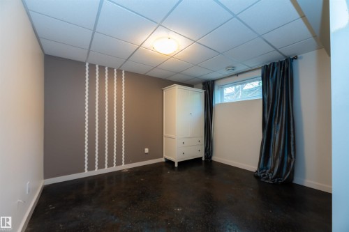 Room featuring dark flooring, light-colored walls, a drop ceiling, and a single window with dark curtains - 704 Wildwood Point(E), Edmonton, AB 