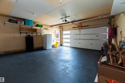 Interior garage space featuring a painted concrete floor, exposed wood ceiling joists, and a white sectional garage door with horizontal frosted panels - 704 Wildwood Point(E), Edmonton, AB 