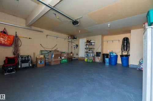 Spacious garage featuring a durable dark grey floor finish, light beige walls, and exposed ceiling beams - 704 Wildwood Point(E), Edmonton, AB 