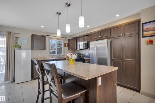 Contemporary kitchen featuring a center island with pendant lighting, rich cabinetry, stainless steel appliances, and tile flooring - 29 1150 Windermere Way, Edmonton, AB 