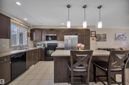Kitchen featuring dark wood-finish cabinetry, light-toned countertops, and a tile backsplash - 29 1150 Windermere Way, Edmonton, AB 