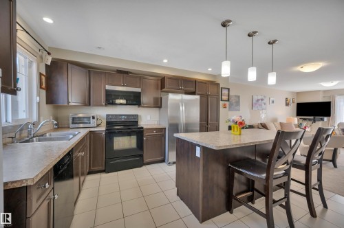 Open-concept kitchen featuring dark wood-finish cabinetry, a stainless steel refrigerator, and a black range with an integrated microwave - 29 1150 Windermere Way, Edmonton, AB 