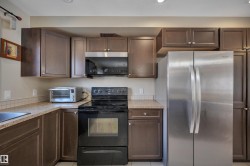 Contemporary kitchen featuring dark wood cabinetry, a stainless steel refrigerator, black range, and an integrated stainless steel microwave - 