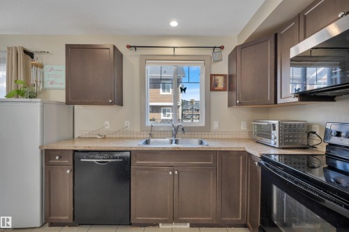 Kitchen with warm-toned cabinetry, a double basin stainless steel sink, and a light-colored countertop - 29 1150 Windermere Way, Edmonton, AB 