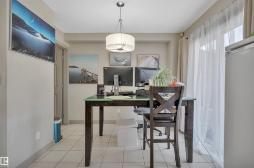 Dining area featuring ceramic tile flooring, a contemporary drum pendant light fixture, a glass-topped table, and a glass-paneled sliding door - 29 1150 Windermere Way, Edmonton, AB 
