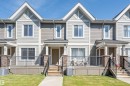 Modern townhome exterior featuring light gray horizontal siding, white trim, prominent gables, a front porch with black metal railings, and stone-clad pillars - 29 1150 Windermere Way, Edmonton, AB 