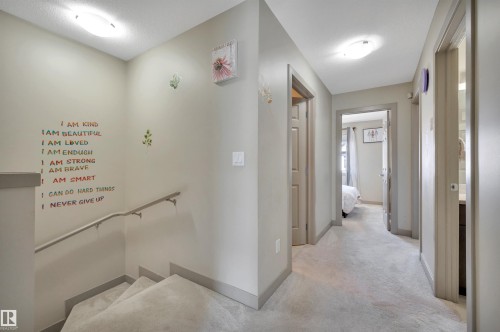 Carpeted staircase with a metal handrail, leading to a carpeted hallway with multiple doorways - 29 1150 Windermere Way, Edmonton, AB 