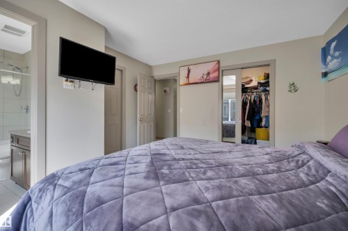 Bedroom featuring a wall-mounted television, a sliding mirrored closet door, and an entryway to a full bathroom with a walk-in shower and single vanity - 29 1150 Windermere Way, Edmonton, AB 