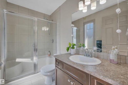 Bathroom featuring a shower-tub combination with glass enclosure, a single vanity with an integrated sink, a large mirror, and tiled walls - 29 1150 Windermere Way, Edmonton, AB 