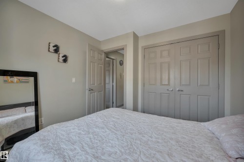 Pendant lighting illuminates this bedroom featuring neutral wall tones, a paneled bifold closet, and a swing door entry - 29 1150 Windermere Way, Edmonton, AB 
