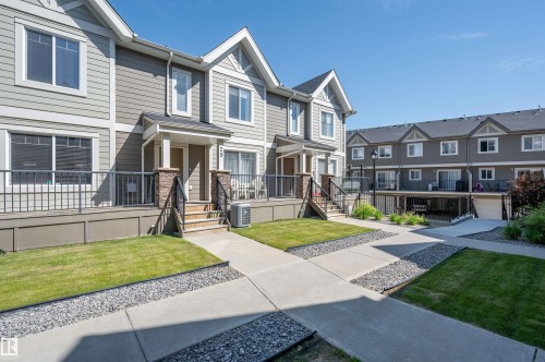 Townhome exterior featuring gray siding, white trim, a covered porch with stone-wrapped columns, and a front patio with dark railings - 29 1150 Windermere Way, Edmonton, AB 
