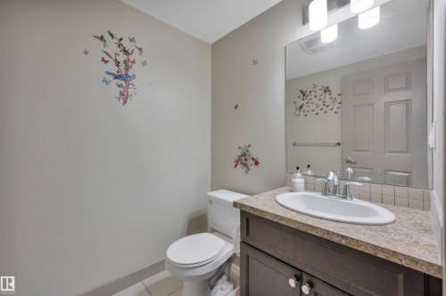 Powder room featuring a white toilet, dark wood-finish vanity with a built-in sink, and a speckled countertop - 29 1150 Windermere Way, Edmonton, AB 