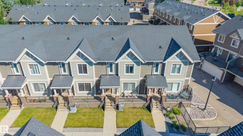 Contemporary townhome development featuring gabled roofs, light grey siding with cream accents, individual front patios, and manicured lawns - 29 1150 Windermere Way, Edmonton, AB 