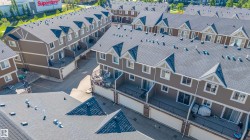 Residential townhome development featuring multiple units with dark shingle roofs, dormer windows, and light tan siding - 