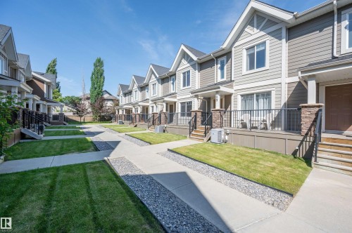 Multi-level townhome featuring a stone-clad entry, covered porch, and a private front yard with manicured lawn - 29 1150 Windermere Way, Edmonton, AB 