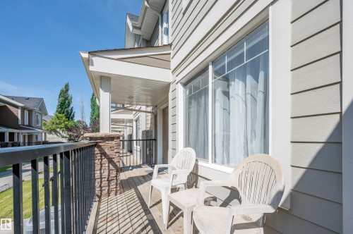 Covered balcony featuring wood-finish decking, black metal railings, and a stone-clad support column - 29 1150 Windermere Way, Edmonton, AB 