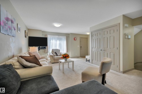 Spacious living area featuring neutral-toned walls, light-colored carpeting, a front entry door, and a built-in closet with double panel doors - 29 1150 Windermere Way, Edmonton, AB 